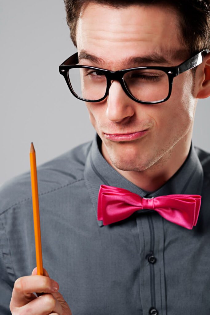 Studente con papillon rosa e matita tra i denti, sguardo ironico davanti al pc, simbolo della discussione tesi online nelle università telematiche