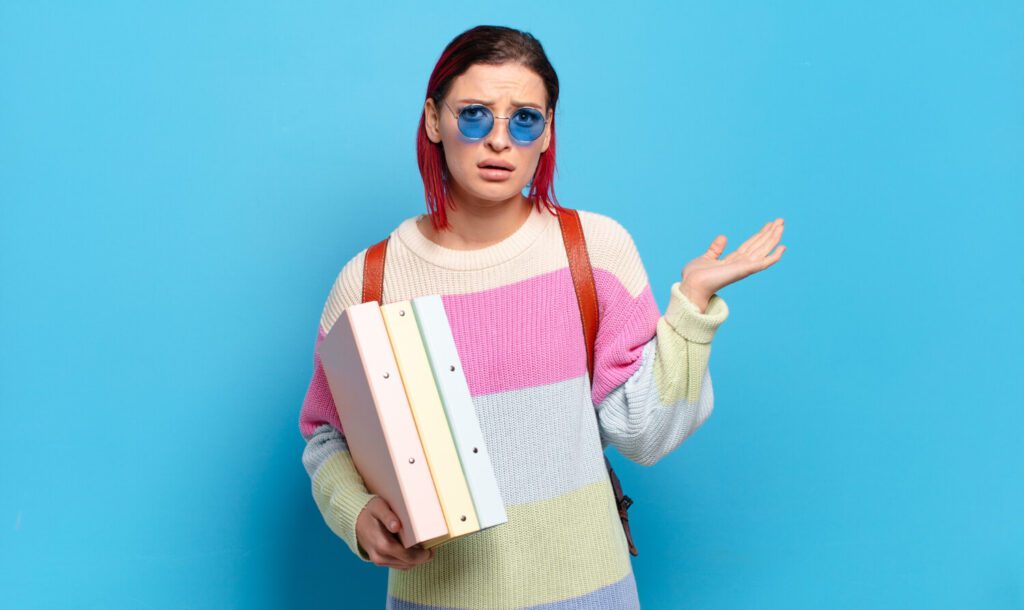 Studentessa confusa con raccoglitori colorati, simbolo della difficoltà nella scelta dell’argomento della tesi