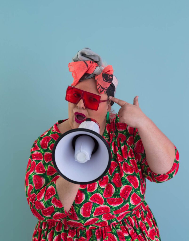 Donna con megafono e look colorato che dà consigli pratici, simbolo ironico dei trucchi per sopravvivere alla discussione della tesi