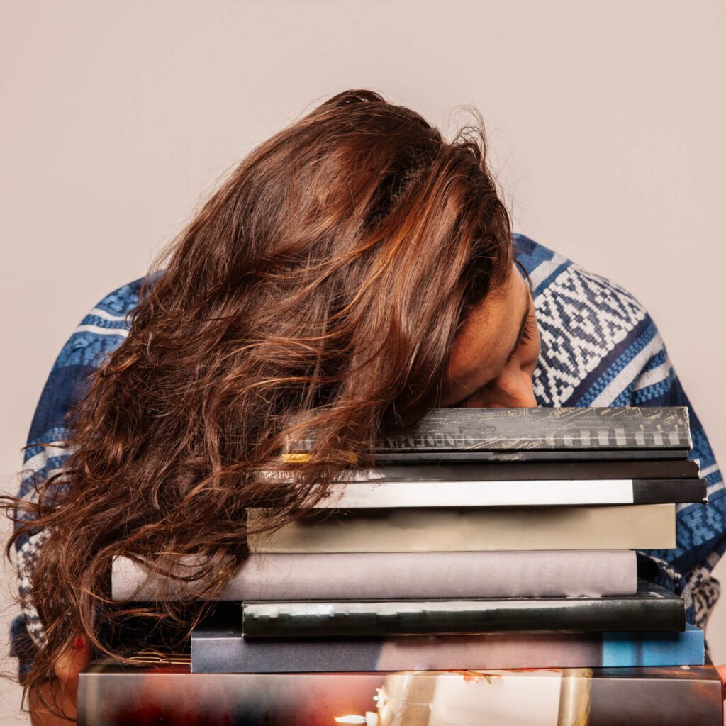 Studentessa stanca appoggiata su una pila di libri per la tesi in economia