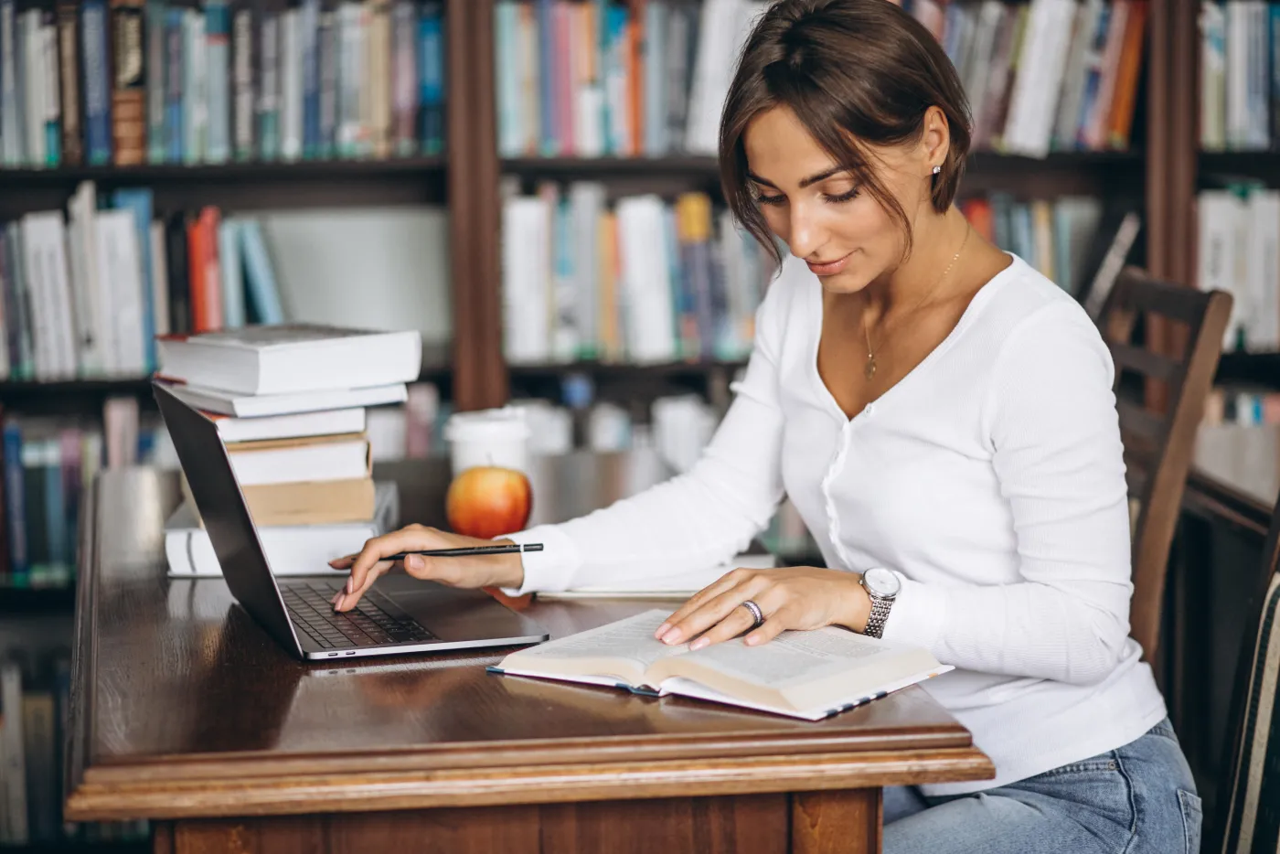 Studentessa universitaria studia la tesi di laurea in biblioteca, con libri e laptop sul tavolo