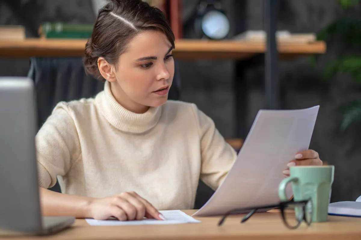 Studentessa che rilegge la tesi stampata accanto al laptop per controllare le parti segnalate dal software antiplagio