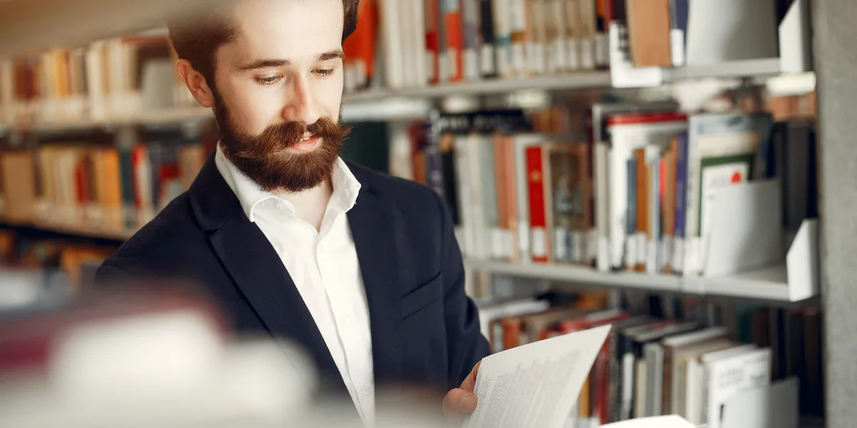 Studente di giurisprudenza che consulta manuali e banche dati in biblioteca per la ricerca della tesi
